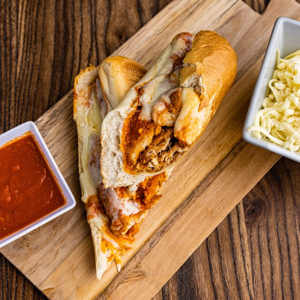Chicken parmesan hero sandwich, cut in half, with marinara sauce and shredded cheese on a wooden board.