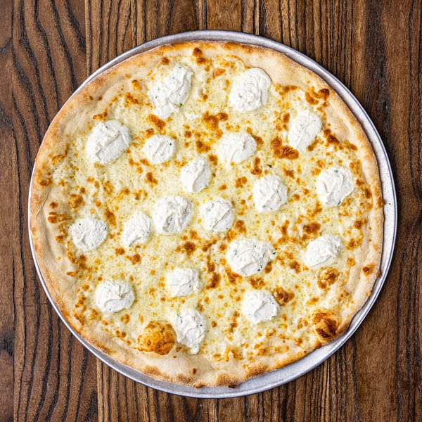 White pizza with dollops of ricotta cheese and golden-brown crust on a wooden table.