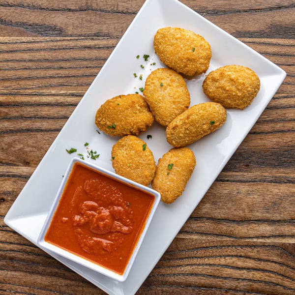 Crispy golden-brown croquettes with green herbs, served with a side of red marinara sauce on a white plate.