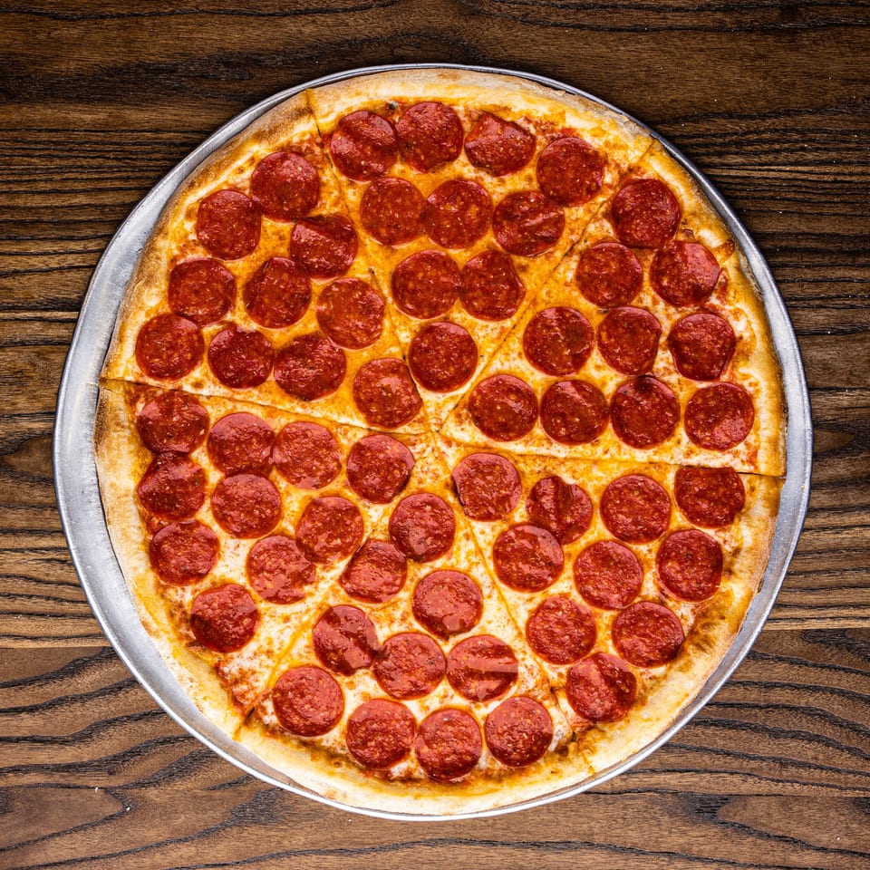A whole pepperoni pizza, sliced into eight pieces, on a metal tray over a wooden table.