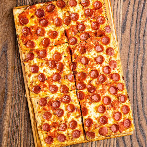 Rectangular pepperoni pizza, cut into squares, on a wooden board.