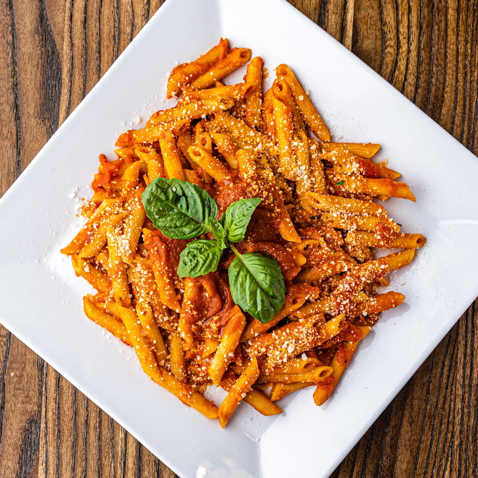 Penne pasta with red sauce, parmesan cheese, and fresh basil on a white square plate.