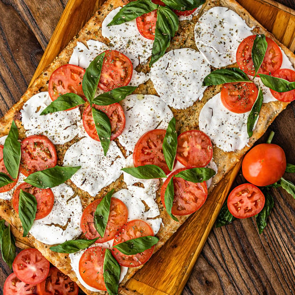 Caprese flatbread with fresh mozzarella, sliced tomatoes, and basil on a wooden board.